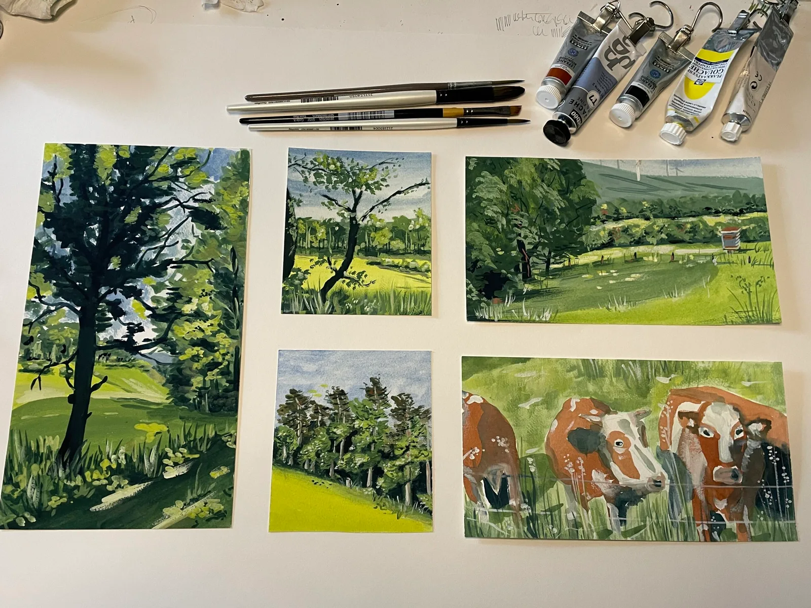 Arbeitsplatz mit Gouache-Malutensilien und sechs Landschaftsskizzen in Grüntönen