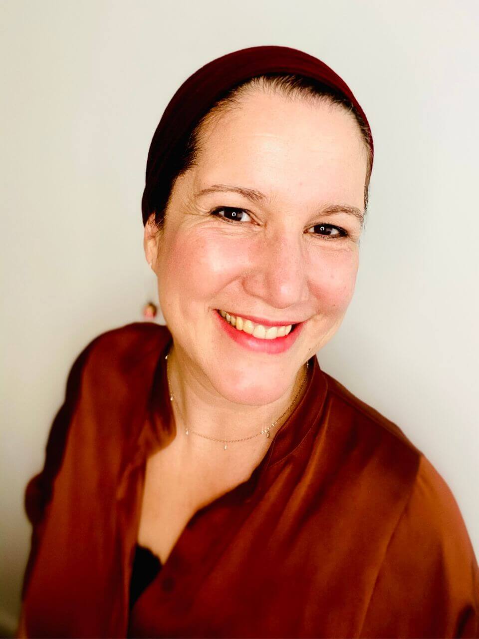 Grenzen-Kurs für Coaches, Berater und Unternehmer 6 Porträt einer lächelnden Frau mit dunklem Haarband und rotbraunem Oberteil vor weißem Hintergrund
