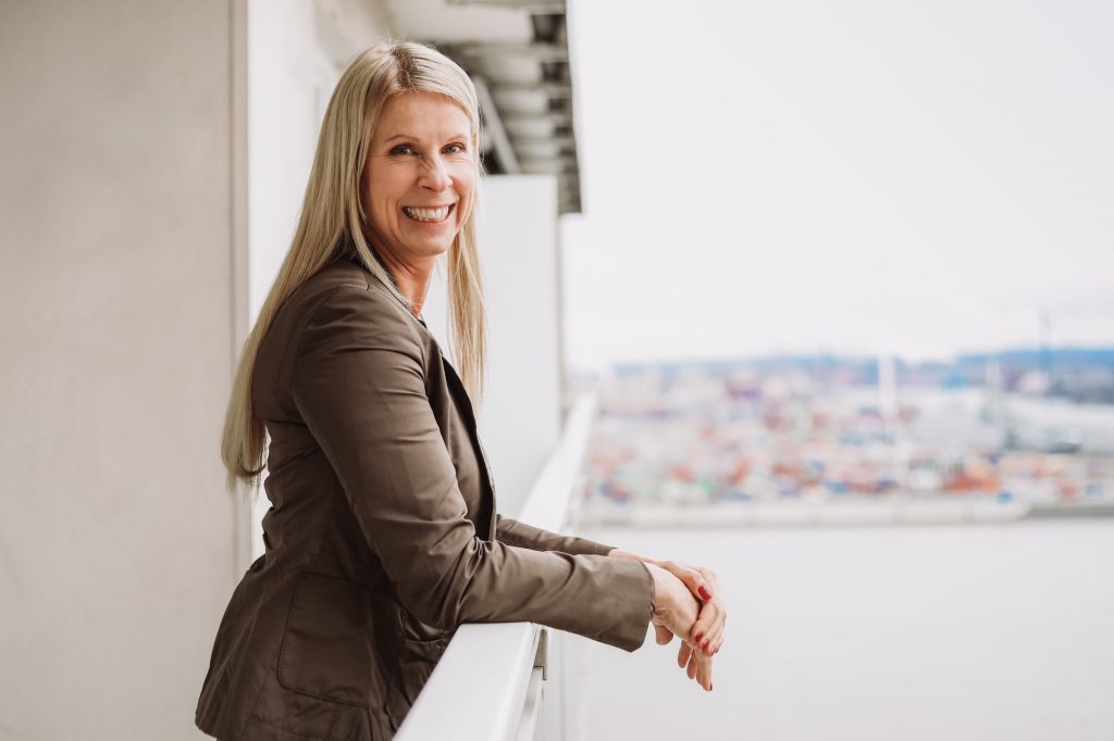 Nicole Freudenberg lächelt an Fenster mit Hafenblick im Hintergrund