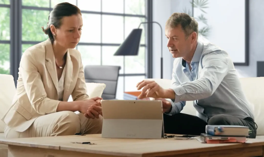Mann und Frau sitzen auf Sofa und besprechen Tablet zusammen im modernen Büro