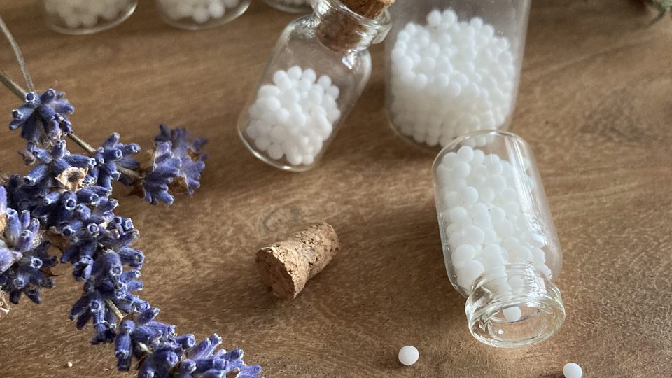 Lavendelblüten neben Gläsern mit weißen homöopathischen Globuli
