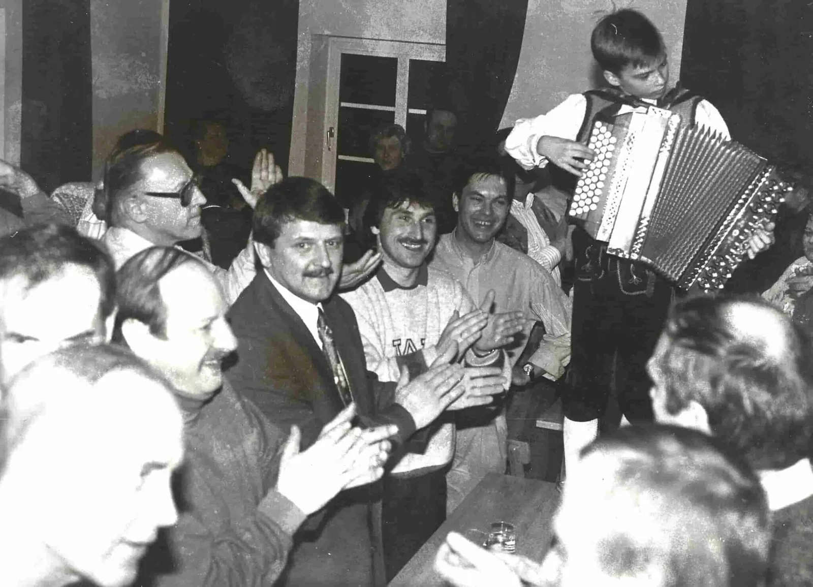 Historische Schwarz-Weiß-Fotografie von Musikant auf Akkordeon bei Tischfeier mit Besuchern