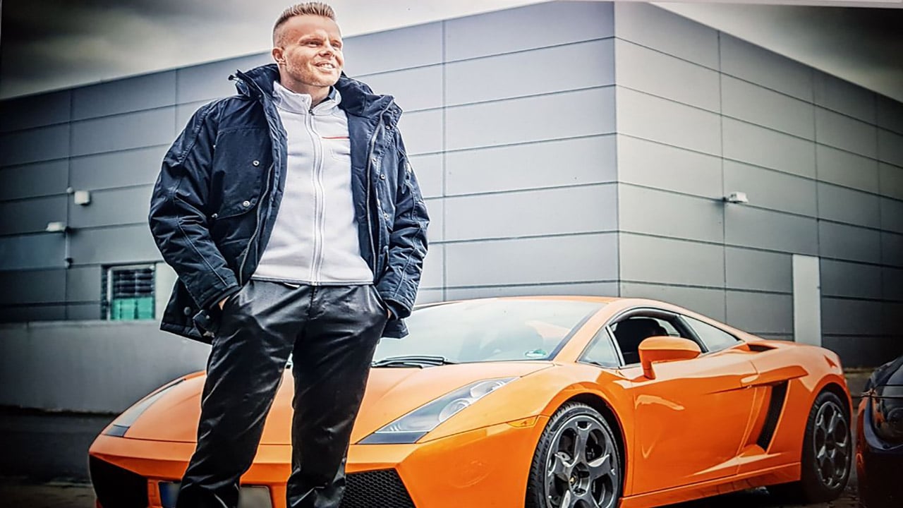 GunnarKessler.com Online Webinar – Seminar zu digitalen Produkten 2 Mann in dunkler Jacke lehnt an orangefarbenem Sportwagen vor modernem Gebäude