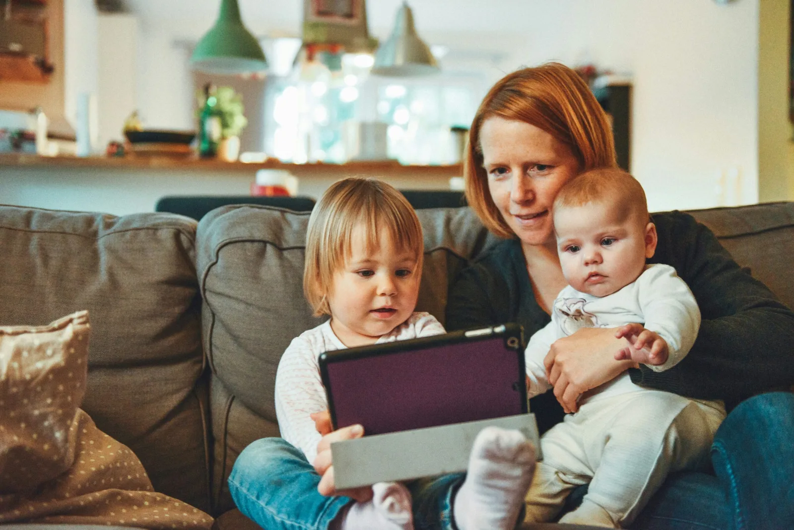 Mutter mit zwei Kleinkindern auf Sofa mit Tablet