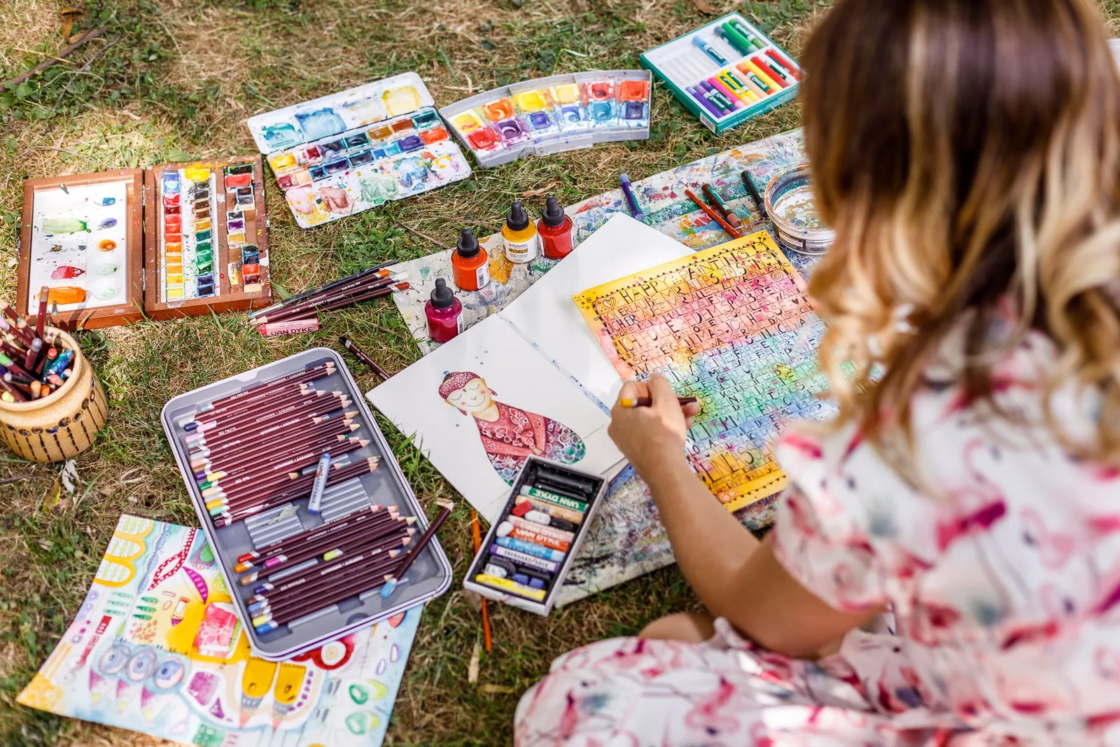 Kind beim Malen mit Farbpaletten und bemaltem Kunstwerk auf Gras sitzend, Rückansicht