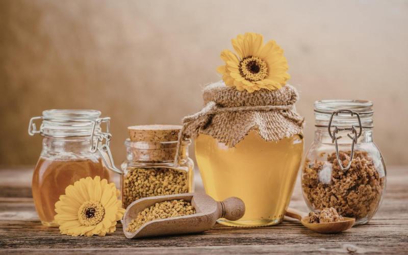 Bienenprodukte mit Honig, Propolis, Pollen in Gläsern und Blüte