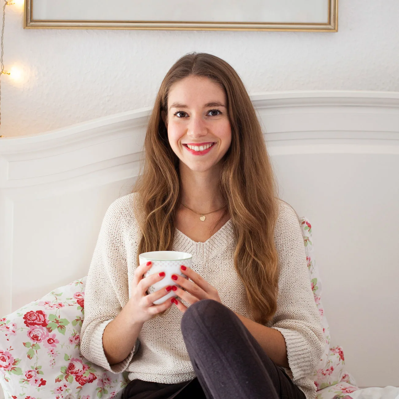 Katharina mit braunen Haaren, weißem Strickpullover, hält Tasse, lächelt