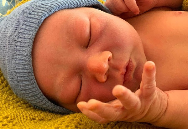 Nahaufnahme schlafendes Neugeborenes in grauer Mütze auf gelbem Tuch