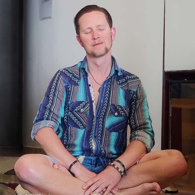 Mann in meditative Haltung sitzend mit geschlossenen Augen und buntem Hemd, spirituelle Praxis