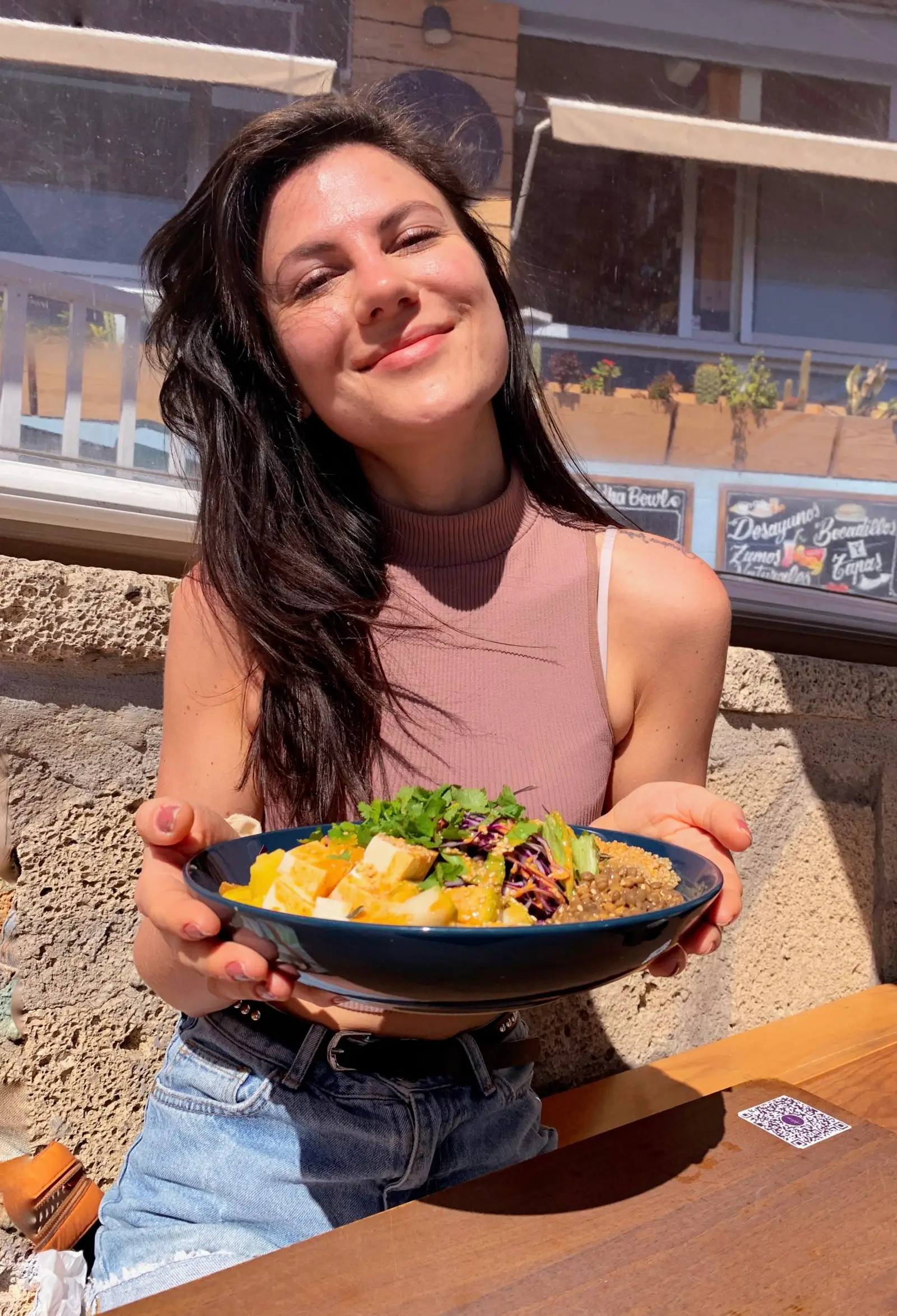 Frau in rosa Top mit Buddha-Bowl und gesundem Essen im Sonnenlicht