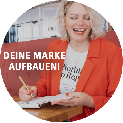 JyotiMa Flak in rotem Blazer schreibend mit Text Deine Marke aufbauen