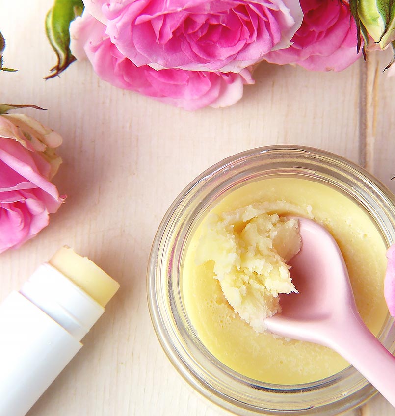 Kosmetik-Creme mit Blüten und rosa Spachtel auf Holzuntergrund