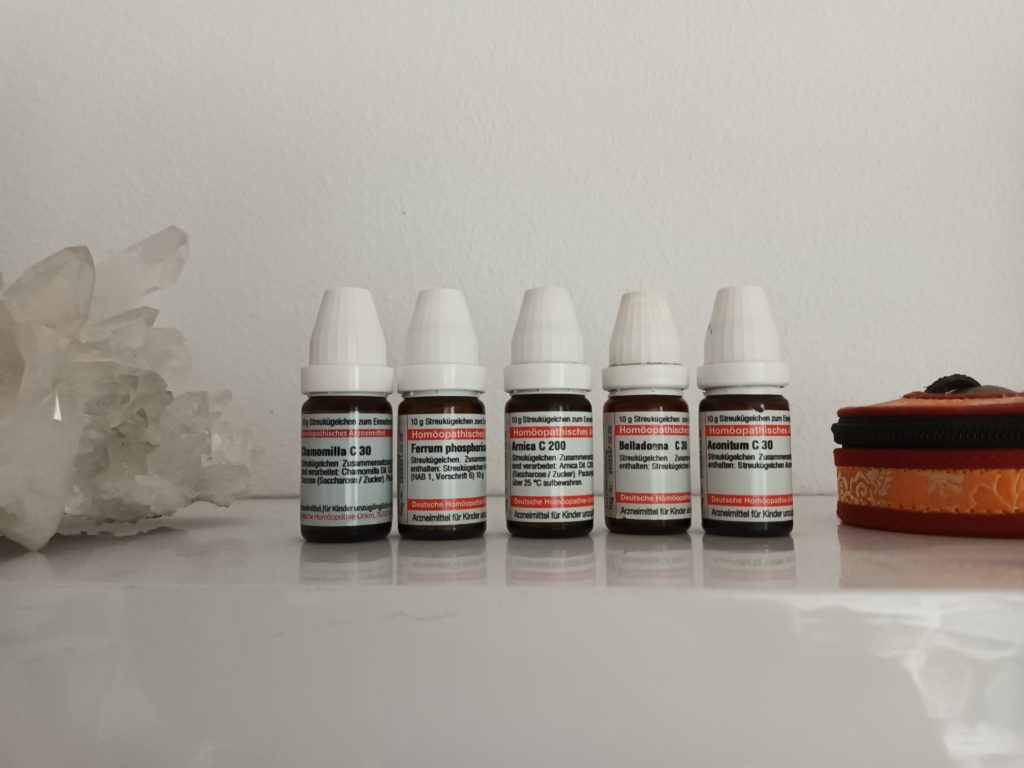 Stillleben mit fünf homöopathischen Globuli-Flaschen, weißer Statue, Holzgrund und Textilie