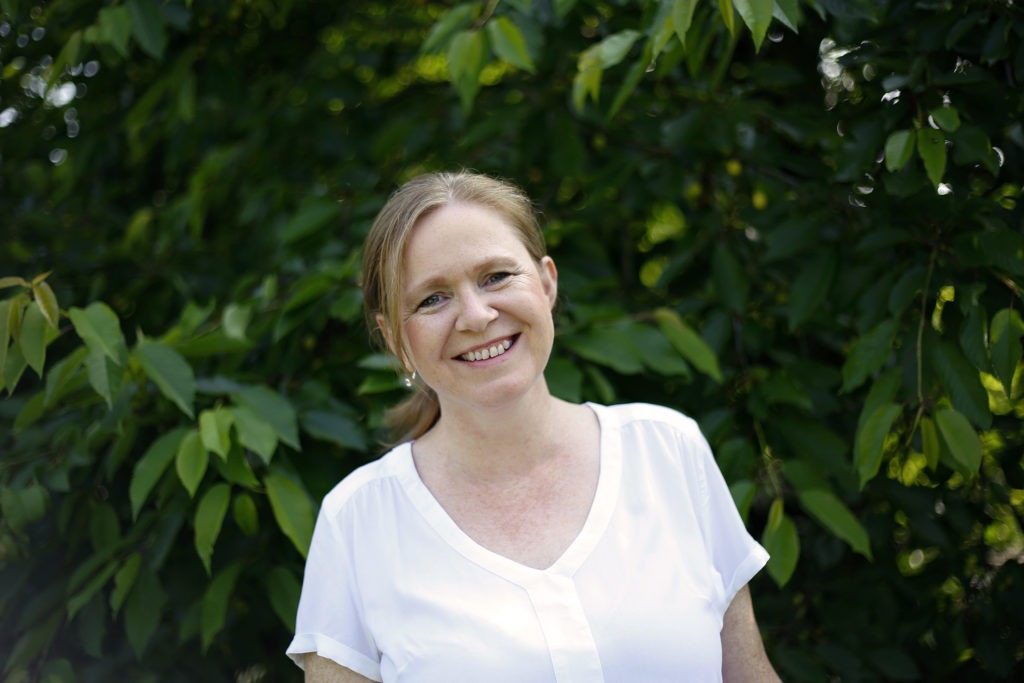 Porträt von Ulrike Schlüter lächelnd vor grünem Laub-Hintergrund