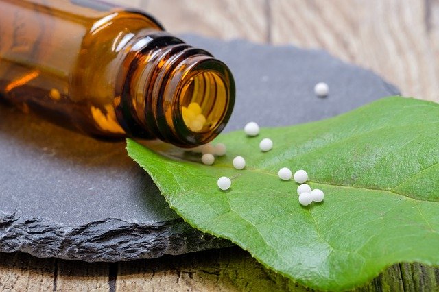 Homöopathische Globuli auf grünem Blatt neben brauner Flasche auf Holzuntergrund