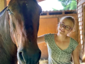 Mädchen mit Brille streichelt einen braunen Pferdekopf im Stall