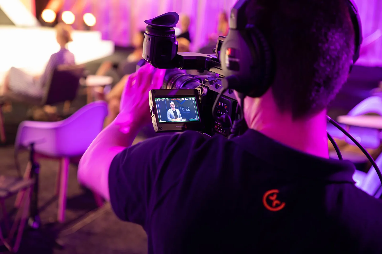 Videokameramann filmt Moderator bei Hybrid-Event mit magentafarbenem Licht