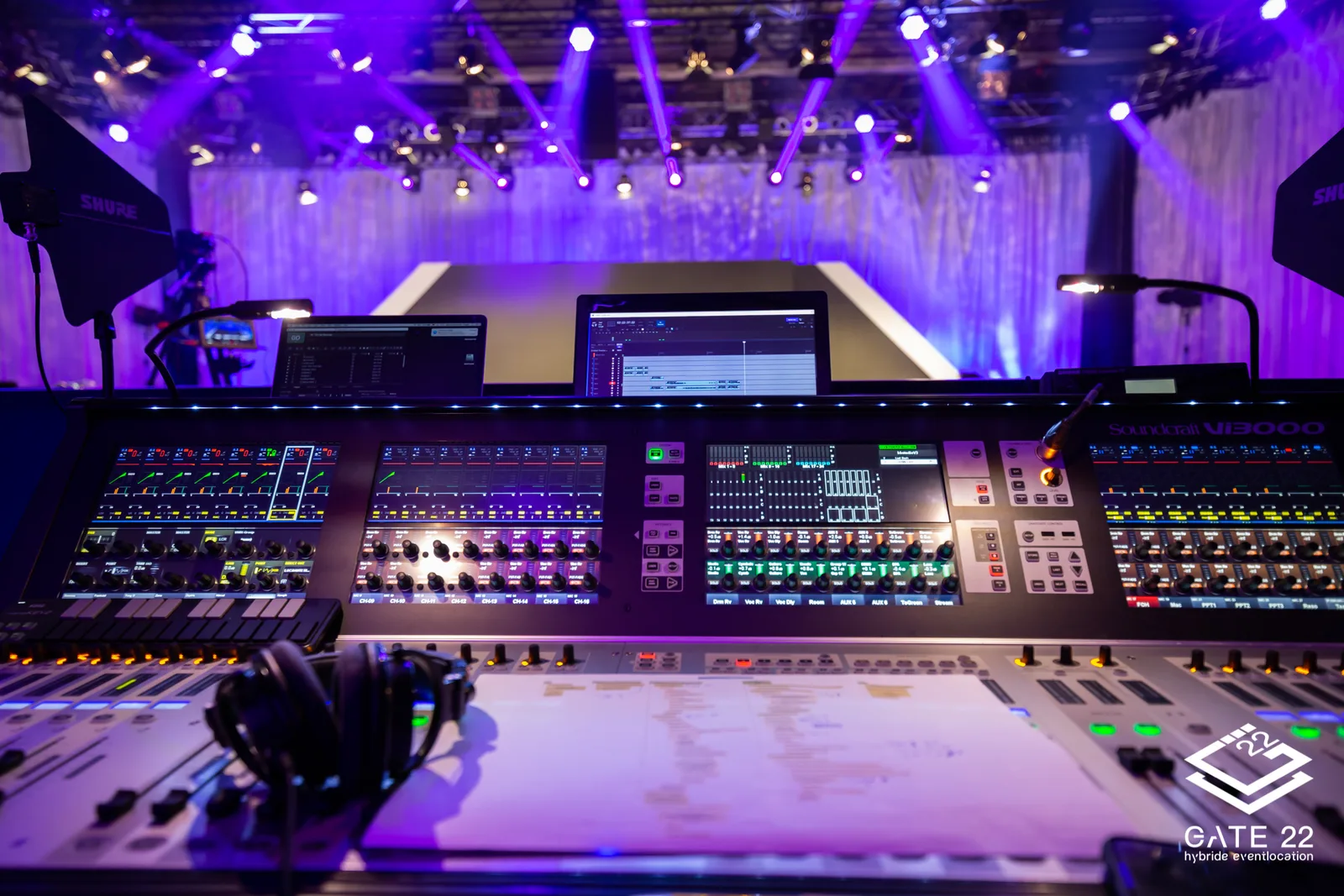 Mixing-Pult und Laptops bei Hybrid-Event mit purpurner Bühnenbeleuchtung