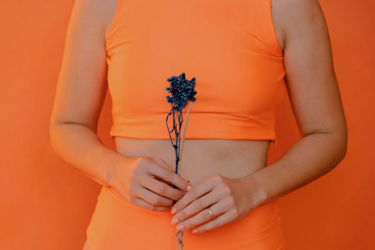 Frau in orange Top hält blaue Blüte vor orangem Hintergrund
