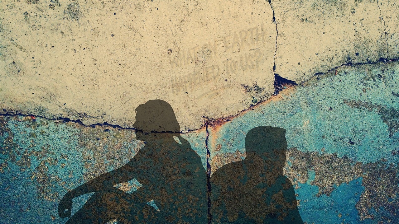 Zwei Personen-Silhouetten an einer Mauer mit Rissen, Liebeskummer-Metapher