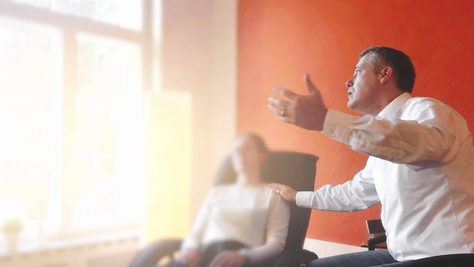 Mann beim Präsentieren vor Publikum in modernem Raum mit orangeroter Wand