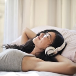Frau mit Kopfhörern liegt im Bett und hört Podcast