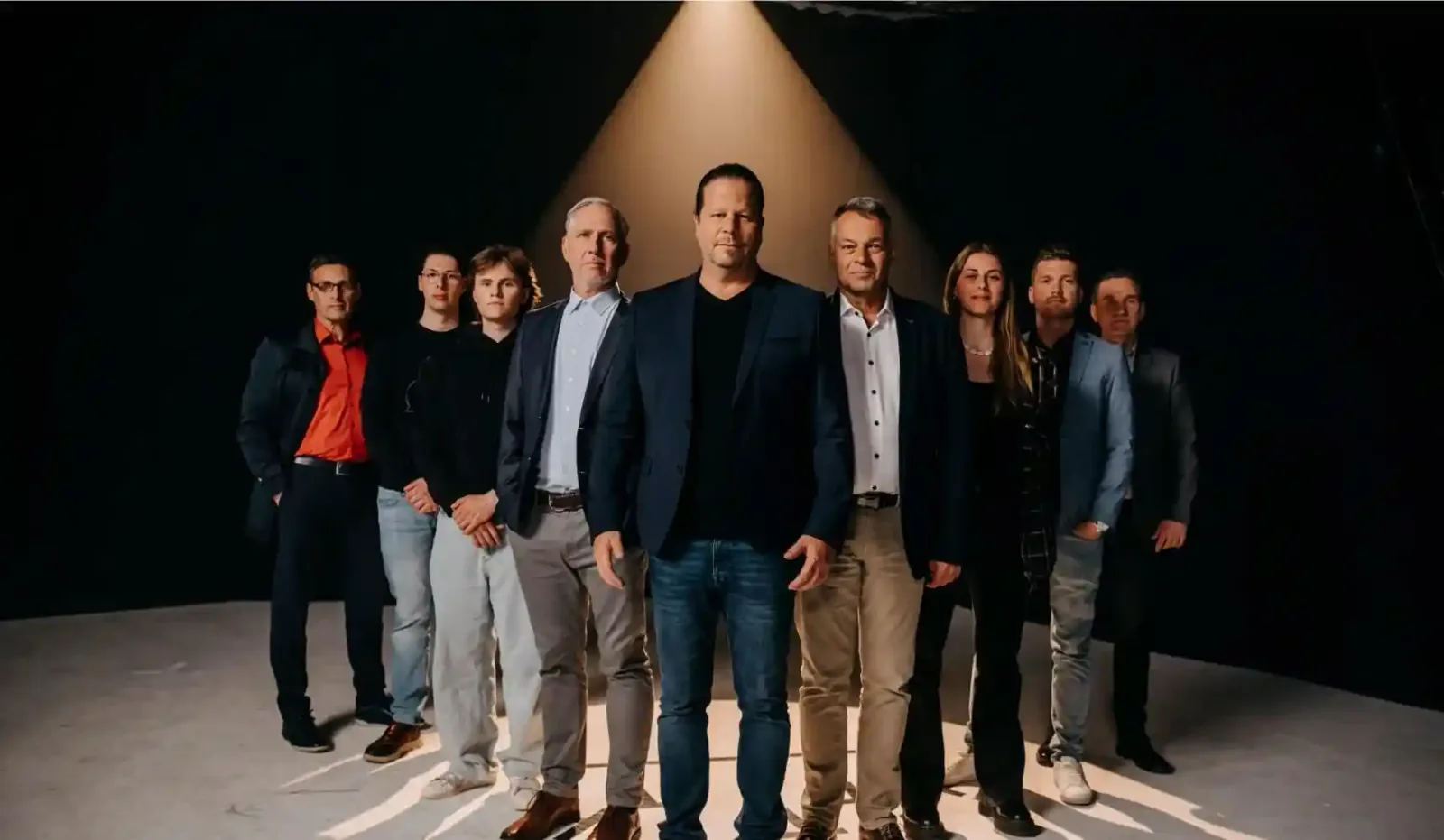 Zehn Personen in Business-Kleidung stehen nebeneinander vor schwarzem Hintergrund mit Spotlight