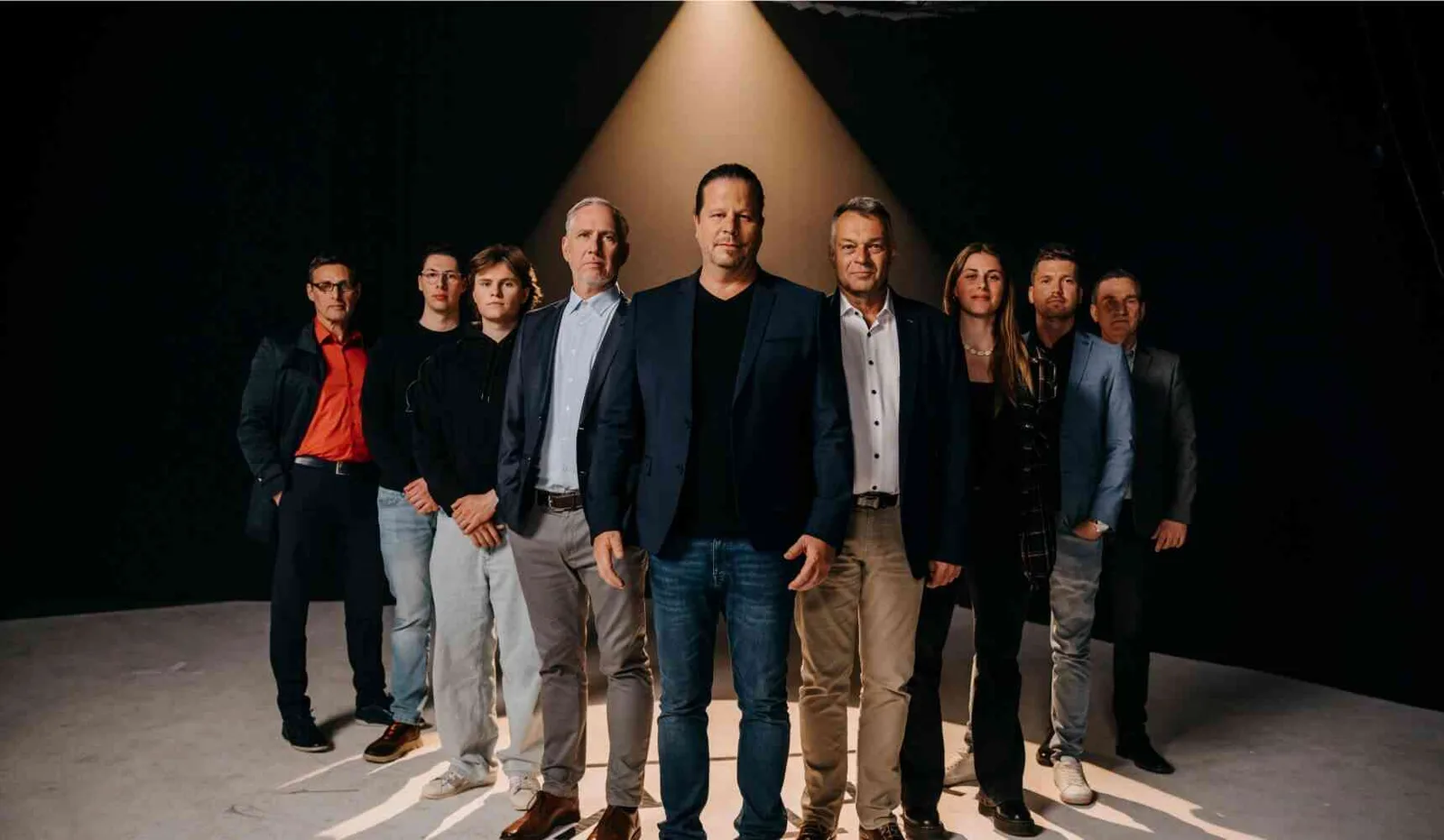Zehn Personen in Business-Kleidung stehen nebeneinander vor schwarzem Hintergrund mit Spotlight
