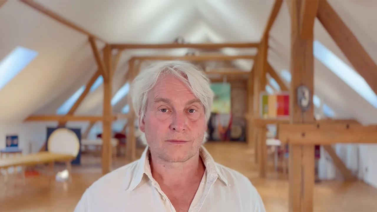Porträt von Uwe Albrecht in Dachraum mit Holzbalken und Farbfeldern, Videostandbild