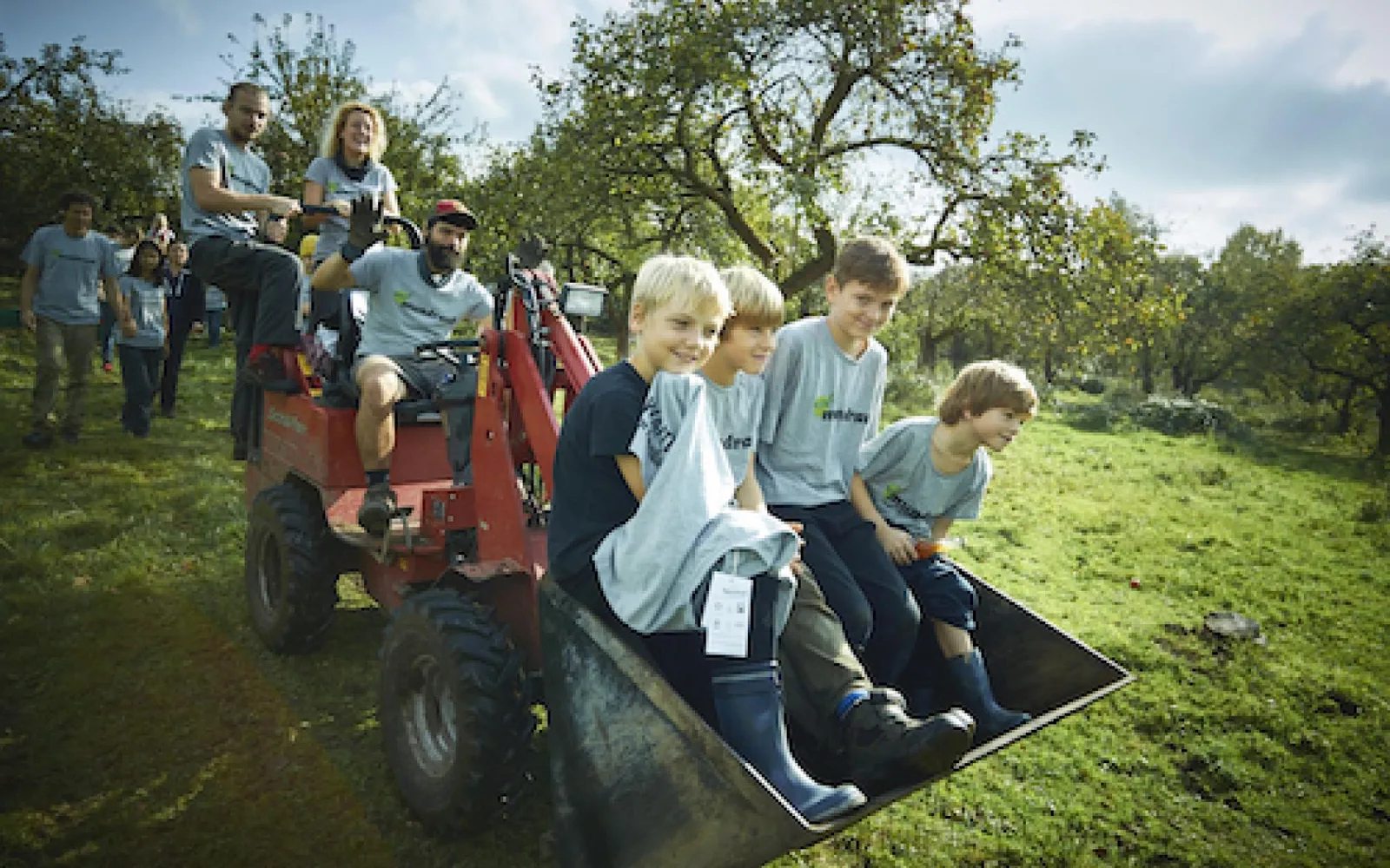 Kinder und Erwachsene bei einer Ernteaktion auf einer Wiese mit Obstkisten und Traktor