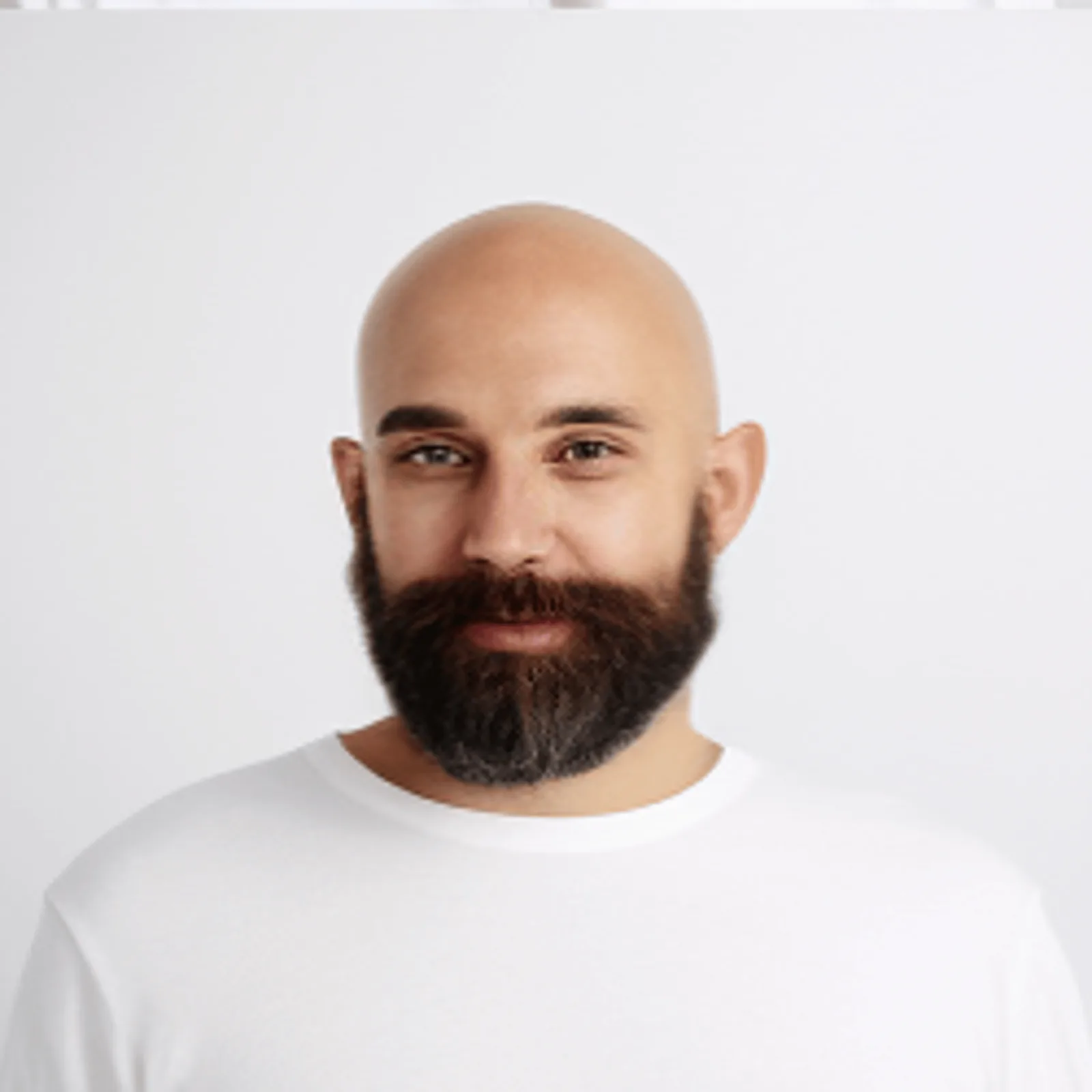 Portrait eines Mannes mit Glatze, dunklem Vollbart, weißem T-Shirt vor neutralem Hintergrund