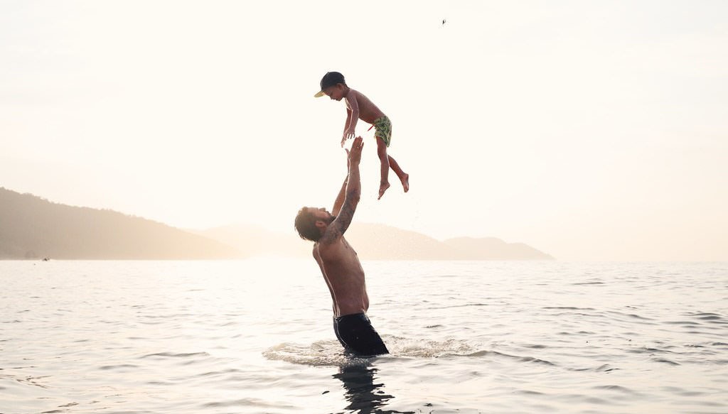Vater wirft Kind im flachen Wasser am Strand in die Luft