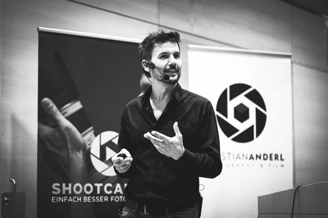 Christian Anderl spricht mit Headset auf Bühne vor Shopcamp und Logo-Banner