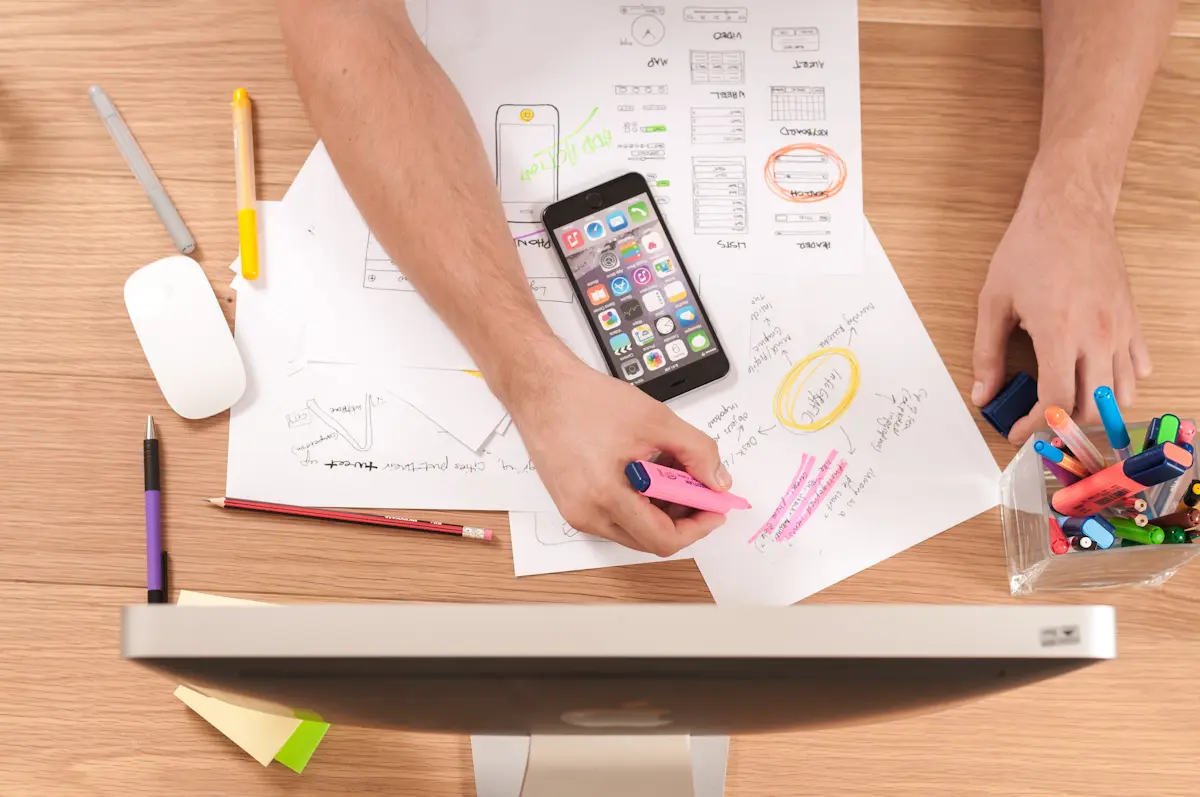 Hände über Schreibtisch mit Skizzen, Smartphone und Designutensilien