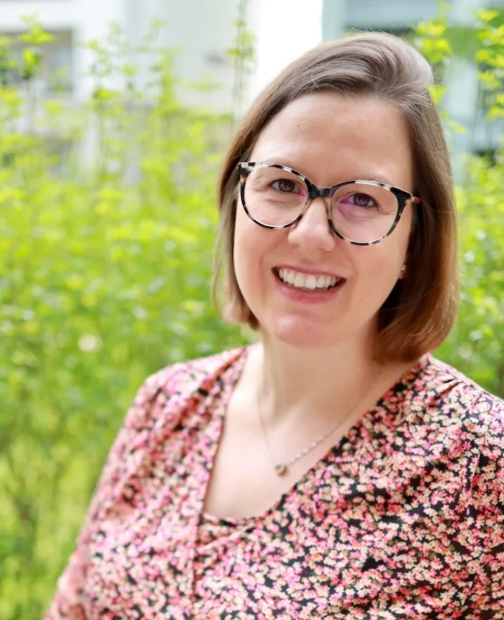 Porträt von Nora Lucia Barta, Frau mit Brille vor grünem Hintergrund