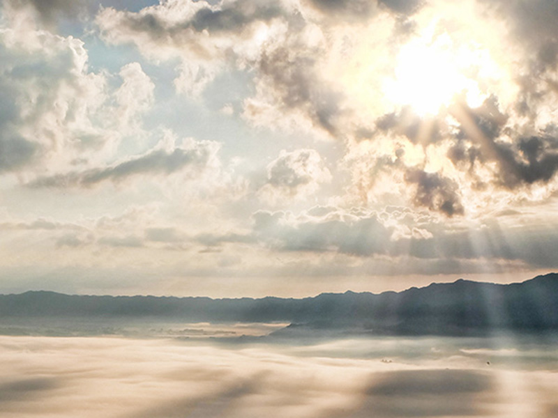 Himmelsszenerie mit Wolken und Sonnenstrahlen über Berglandschaft und Nebel