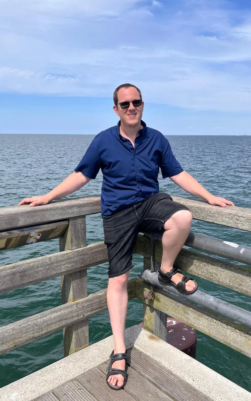 Porträt von Matthias Schindler am Meer auf Holzsteg mit Sonnenbrille