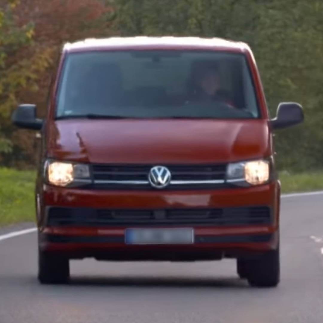 Roter VW T6 Transporter Frontansicht auf Straße mit Bäumen im Hintergrund