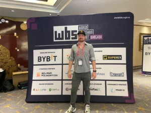 Mann vor World Blockchain Summit Bangkok Sponsoren-Backdrop mit Bybit und Superex Logos