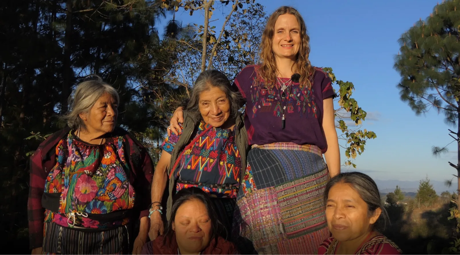 Junge Frau mit zwei älteren Frauen in bunter traditioneller Maya-Kleidung vor Berglandschaft