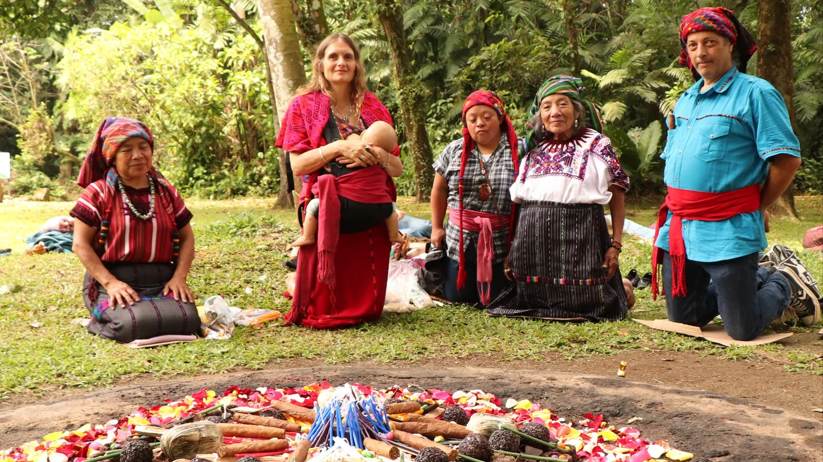 Gruppe von Menschen in traditioneller indigener Kleidung kniet vor Lagerfeuer im Wald