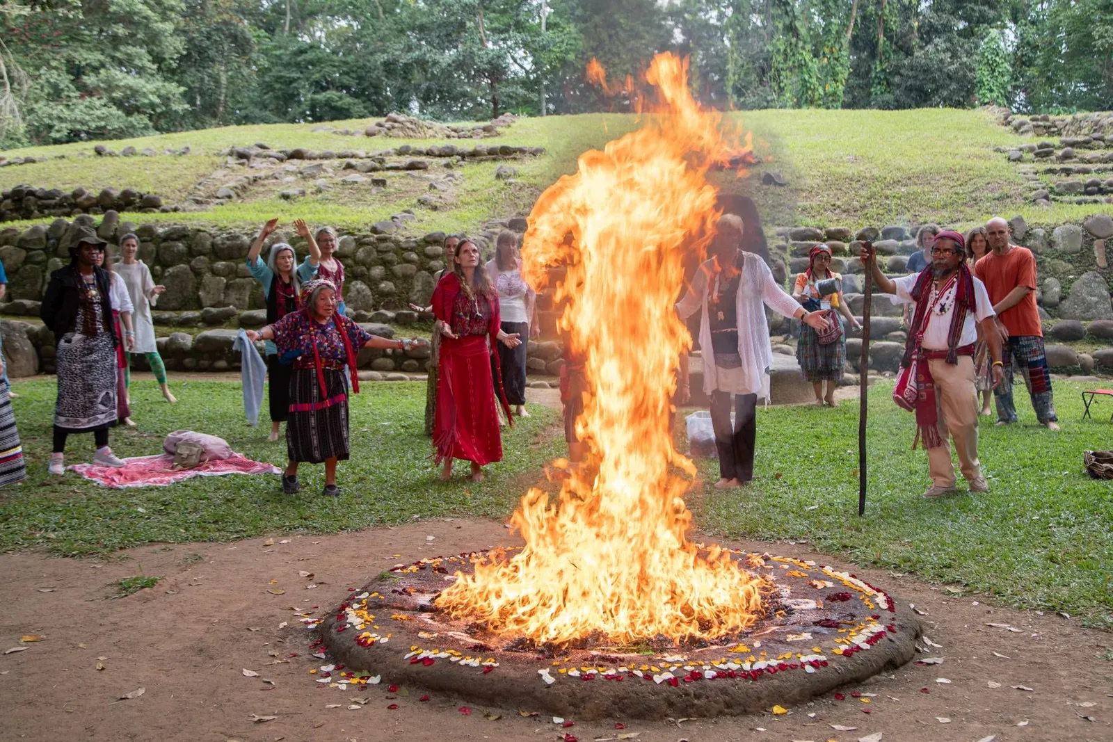 Großes loderndes Lagerfeuer umgeben von Menschen in traditioneller Kleidung bei archäologischer Stätte