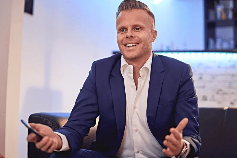 Gunnar Kessler lächelt in dunklem Blazer und weißem Hemd vor Fenster mit Stadtblick