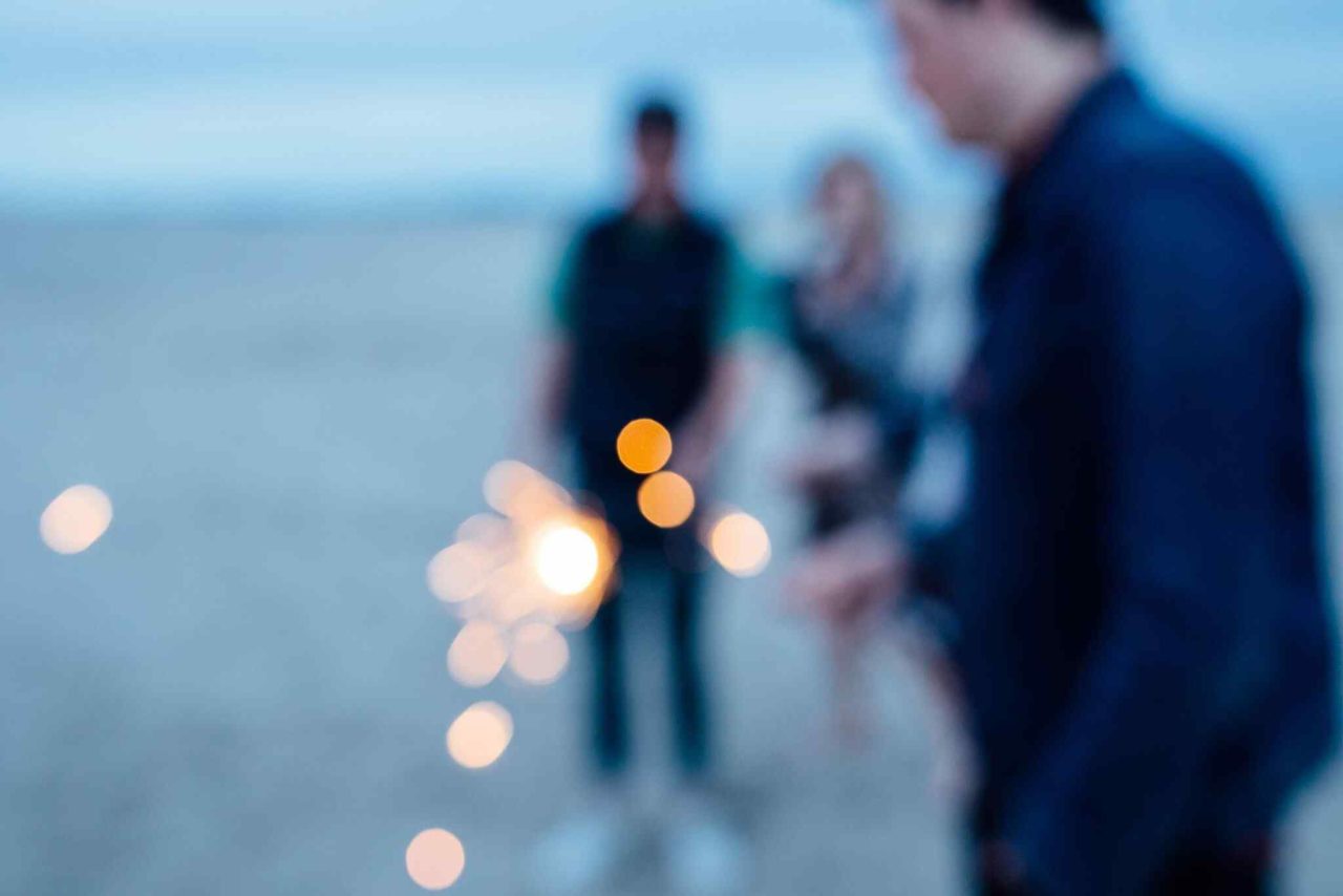 Verschwommene Aufnahme von Personen am Wasser mit Bokeh-Lichtern in Dämmerung