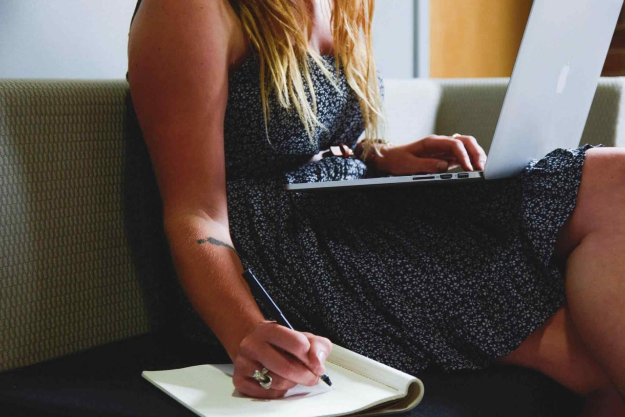 Frau mit blonden Haaren sitzt auf Sofa und arbeitet am Laptop