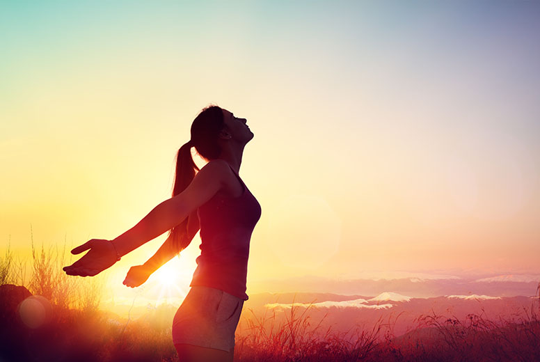 Silhouette einer Frau mit ausgebreiteten Armen bei Sonnenaufgang in einem Feld