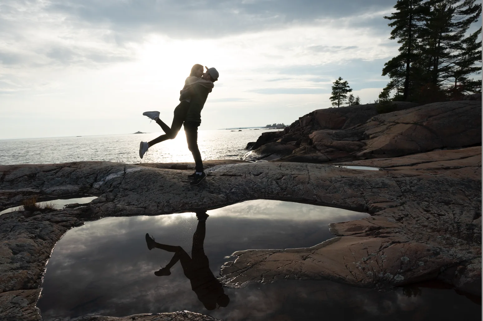 Paar springt auf Felsen am Meer, Silhouette gegen Wasser, kühle natürliche Töne