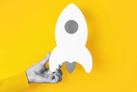 Investieren für Einsteiger – E-Book zur Geldanlage 4 Hand hält weiße Rakete auf gelbem Hintergrund, Investmentstart-Symbolbild