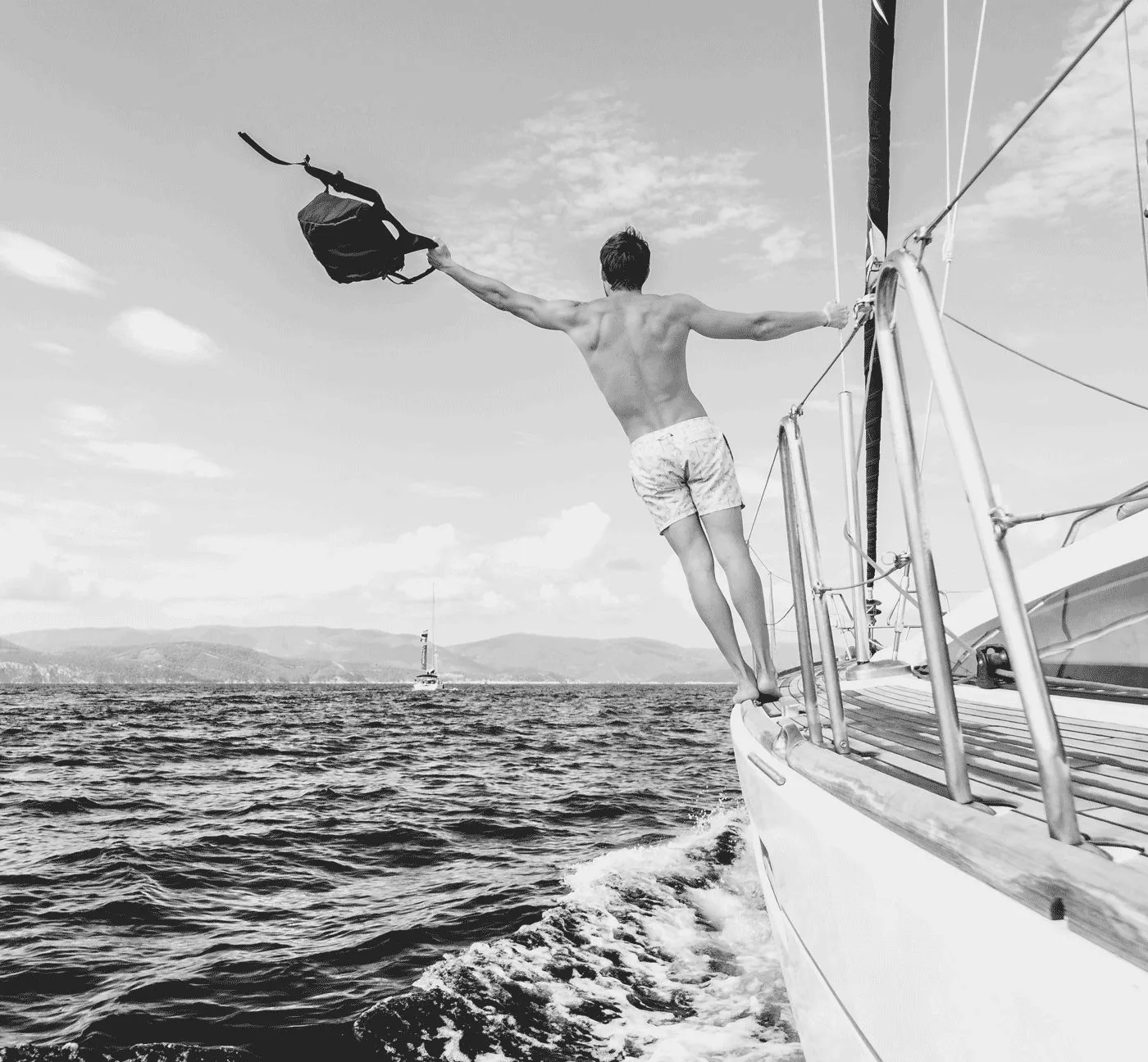 Mann auf Segelboot wirft Hut in die Luft über dem Meer, Schwarz-Weiß-Fotografie