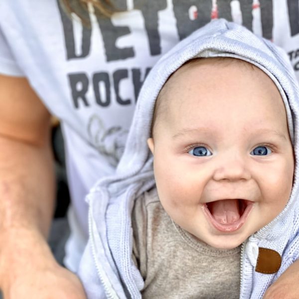 Porträt eines lachenden Babys mit blauem Häubchen in den Armen eines Erwachsenen